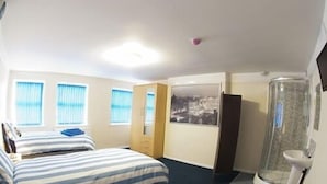 A hotel room with two beds, a shower, a toilet, and a window with blinds. - Liverpool Gateway Inn (Liverpool)