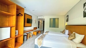 A hotel room with a large bed, wooden shelving, a flat-screen TV, and a small seating area. - Dekuta Hotel (Kuta)