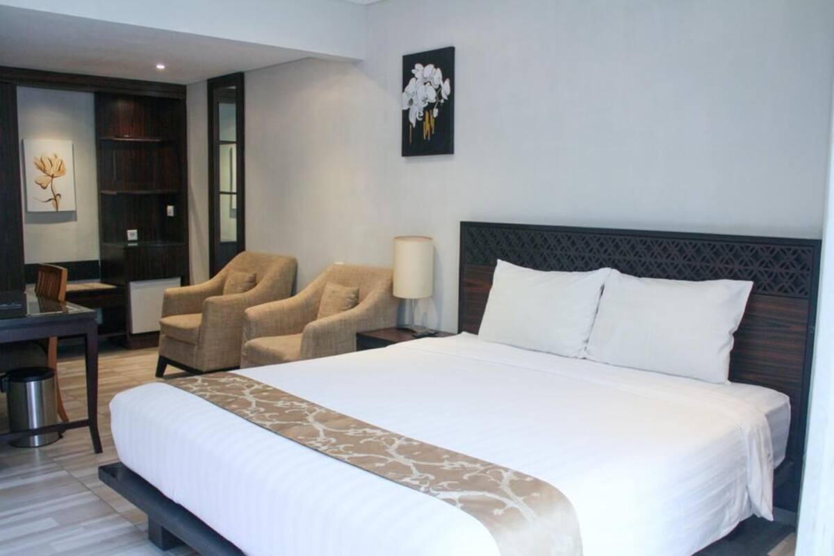 A hotel room with a large bed, two armchairs, a desk, and a trash can.