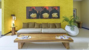 A living room with a yellow wall, a white sofa, a coffee table, and a painting. - Dekuta Hotel (Kuta)