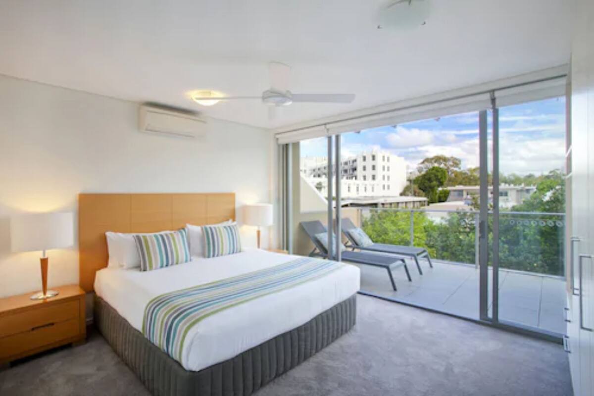 Une chambre d’hôtel moderne dotée d’un grand lit, d’une table de chevet, d’un ventilateur de plafond et d’un balcon offrant une vue sur la ville.