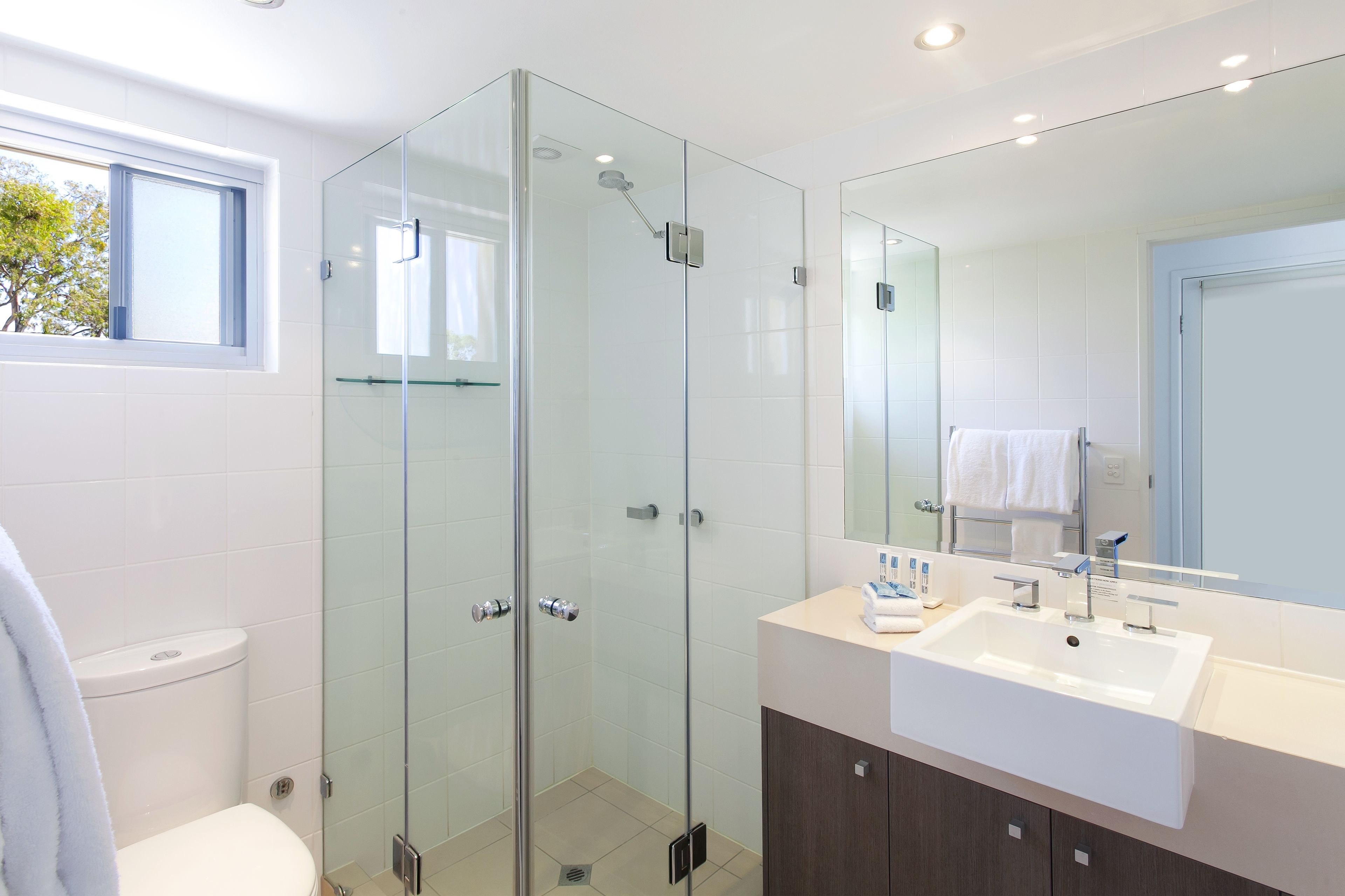 Une salle de bain moderne avec une douche à parois de verre, un lavabo blanc et un grand miroir.