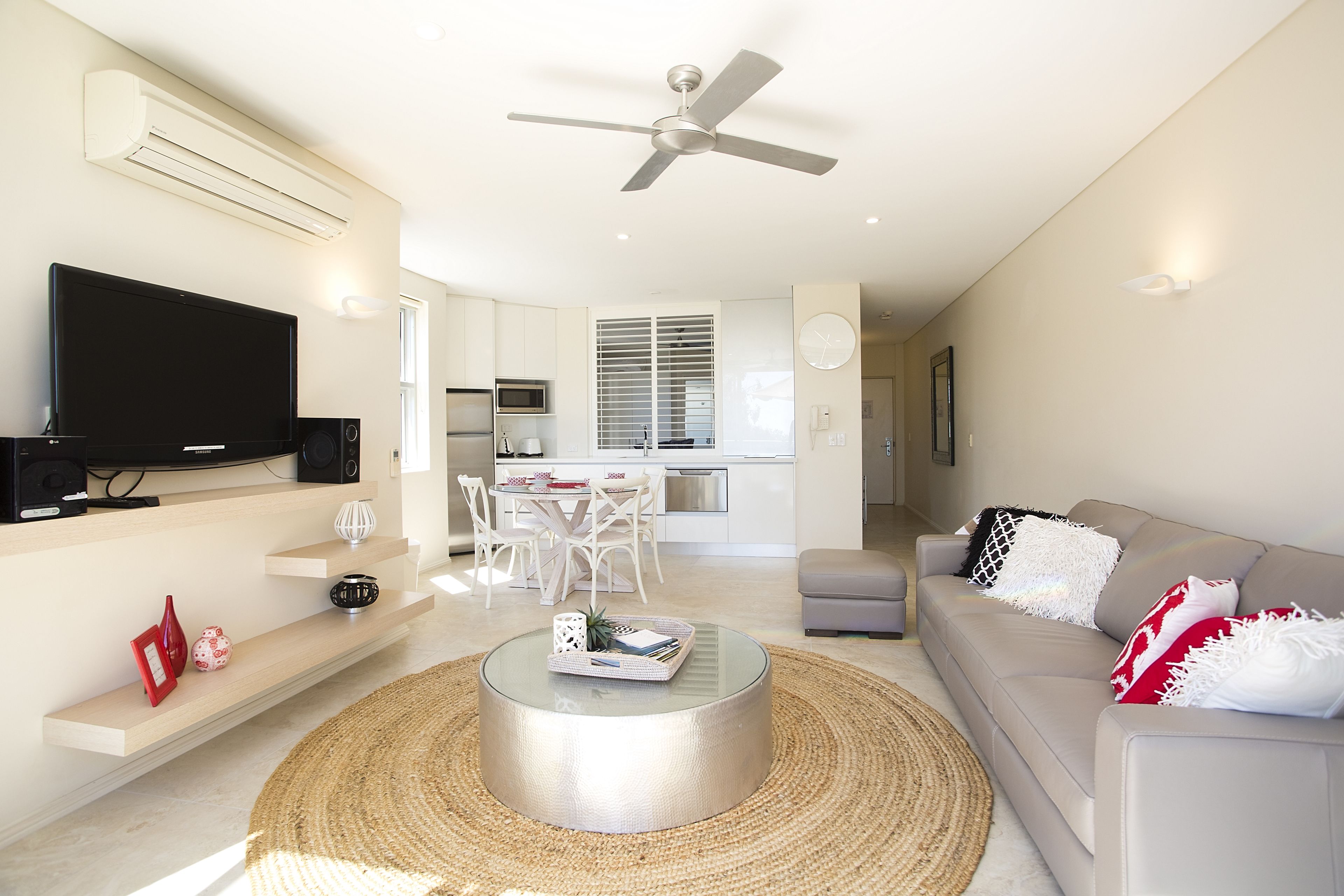 A modern living room with a flat-screen TV, a round coffee table, and a sofa with decorative pillows.