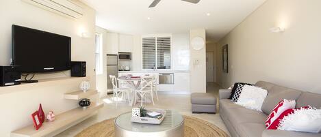 A modern living room with a flat-screen TV, a round coffee table, and a sofa with decorative pillows.