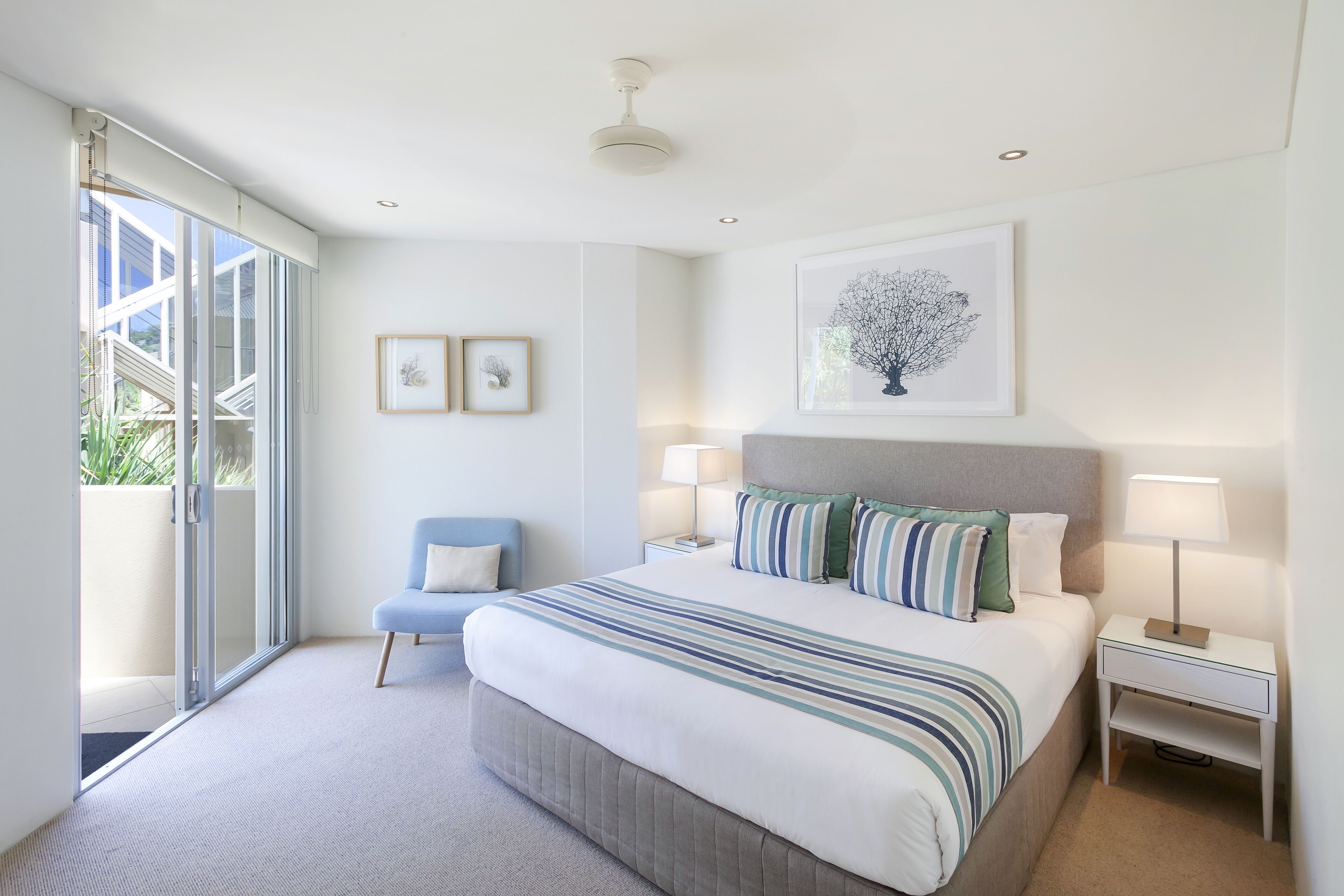 A modern bedroom with a large bed, two bedside tables, a chair, and a sliding glass door leading to a balcony.