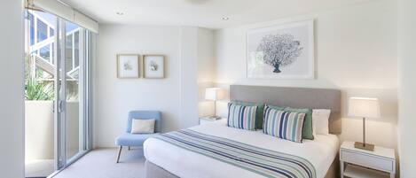 A modern bedroom with a large bed, two bedside tables, a chair, and a sliding glass door leading to a balcony.