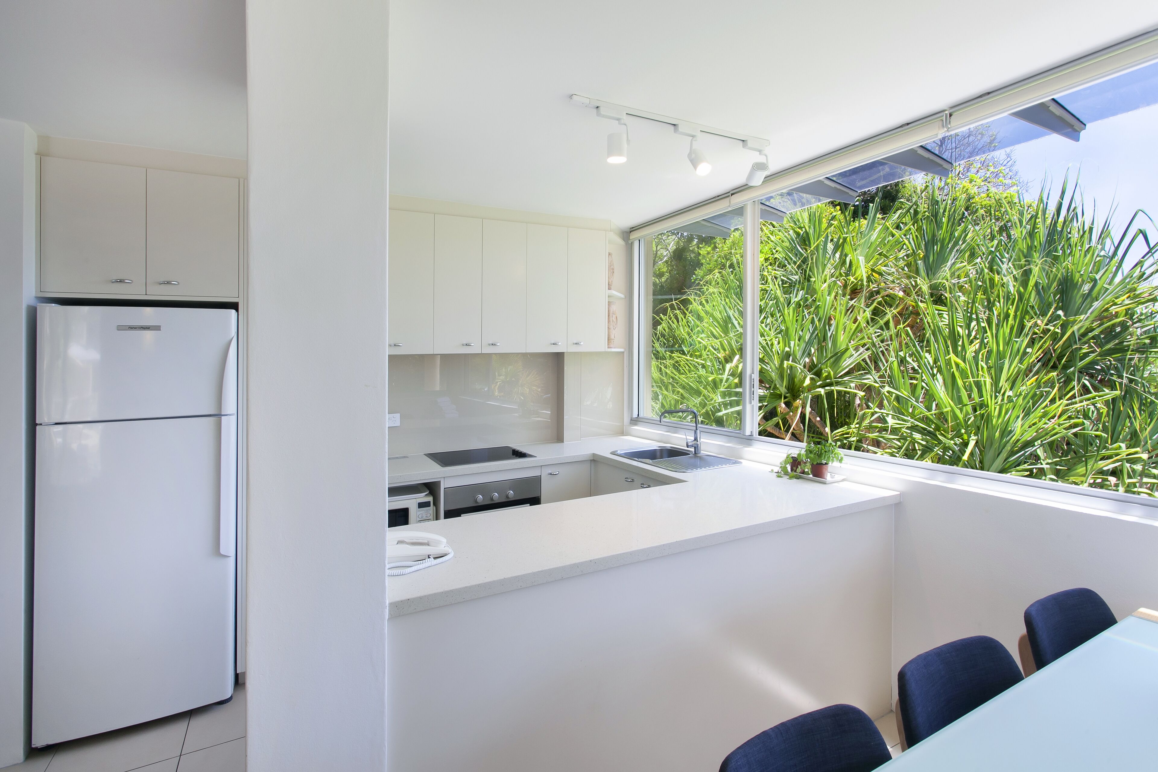 A modern kitchen with white cabinets, a built-in oven, and a large window overlooking greenery.