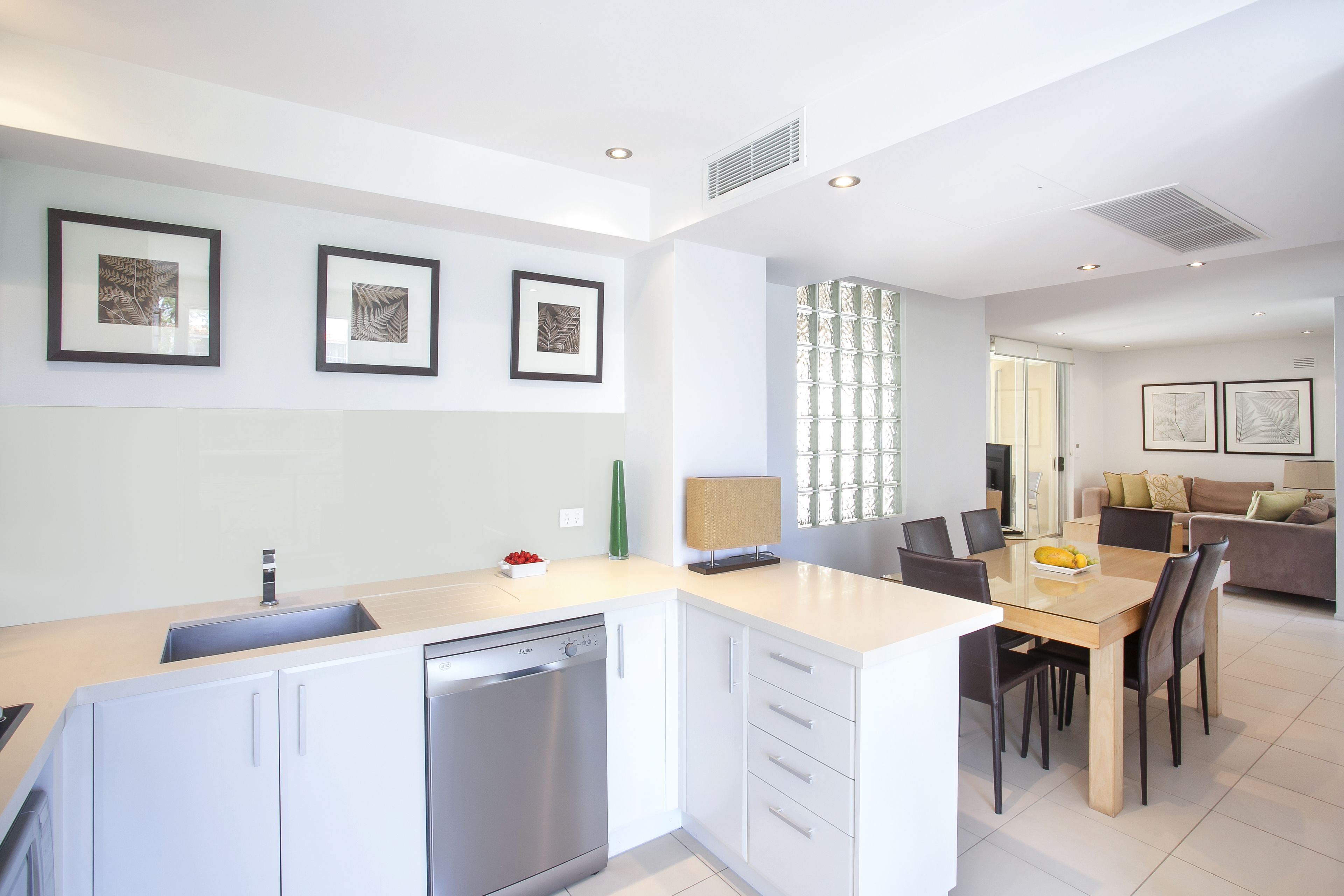 A modern kitchen with white cabinetry, a dishwasher, and a dining area with a table and chairs.
