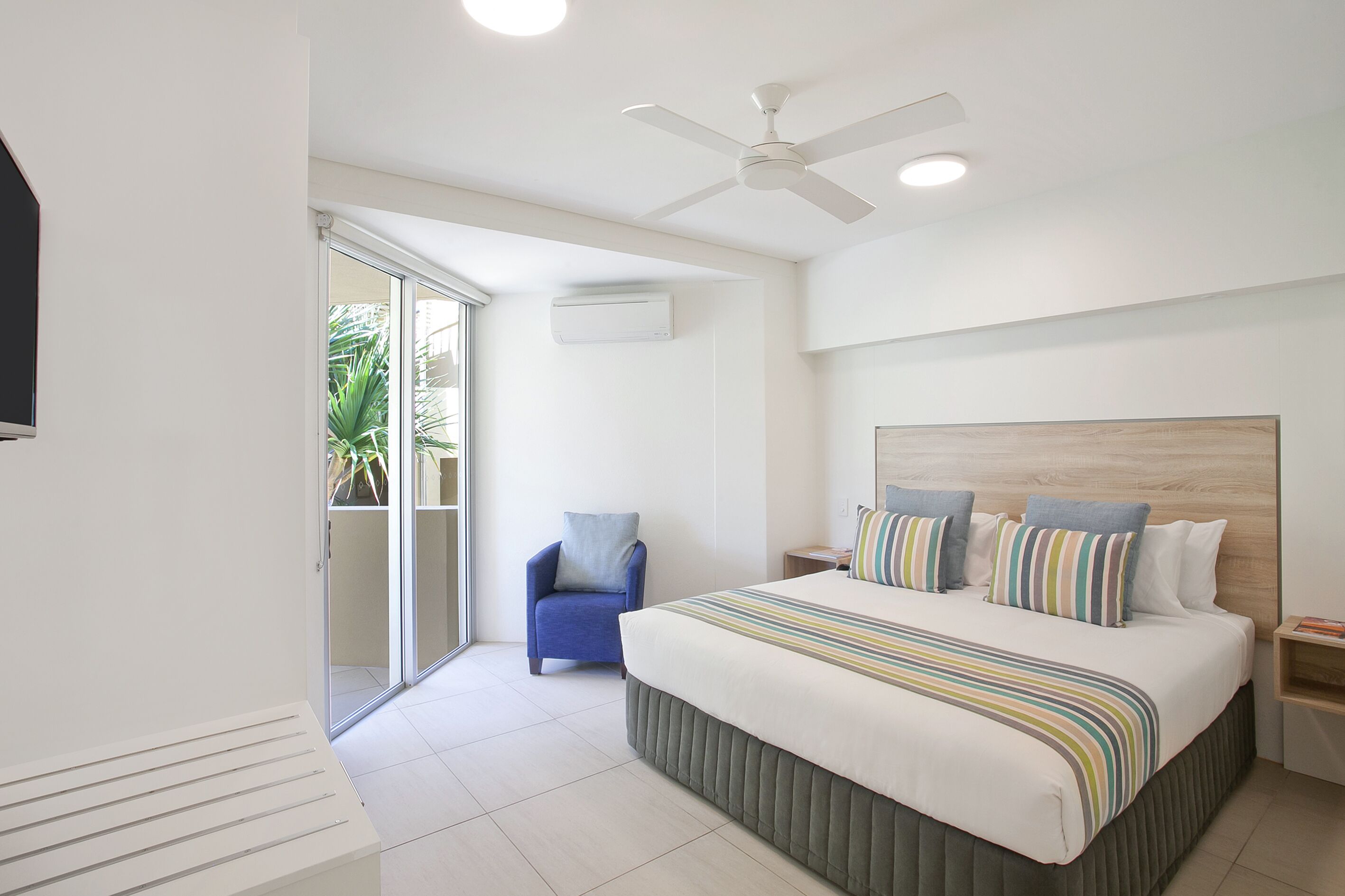 Een moderne hotelkamer met een groot bed, een plafondventilator, een airconditioning en een kleine fauteuil, met uitzicht op de omgeving.