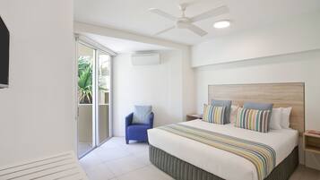 Een moderne hotelkamer met een groot bed, een plafondventilator, een airconditioning en een kleine fauteuil, met uitzicht op de omgeving.