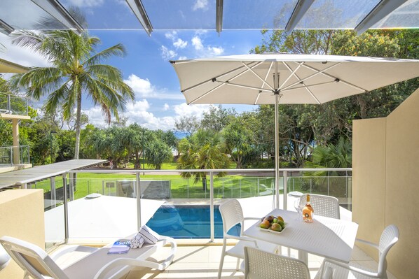 Ein Balkon mit Pool, weißen Möbeln und einem großen Sonnenschirm.