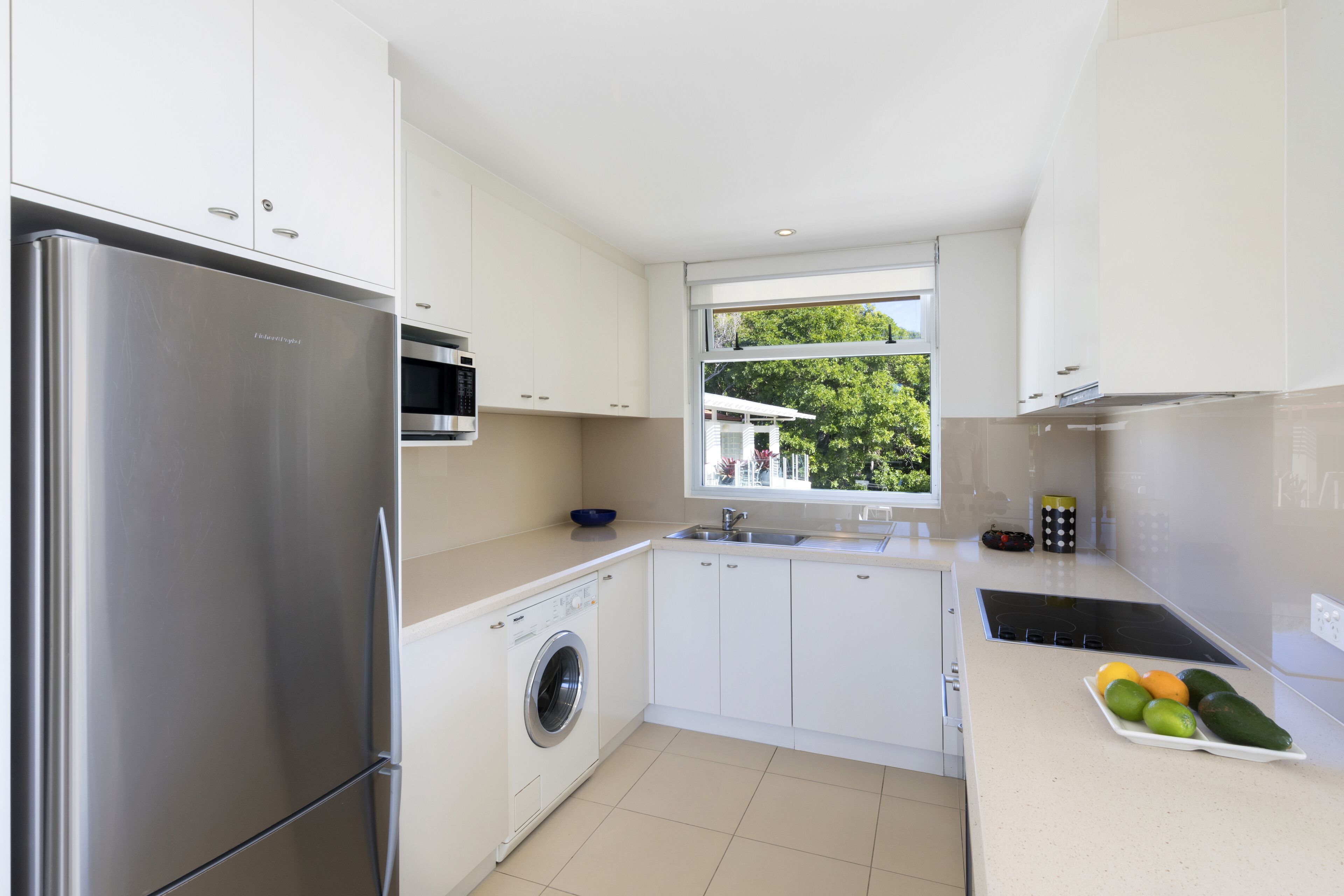 A modern kitchen with white cabinets, stainless steel appliances, a washing machine, and a fruit tray on the counter.