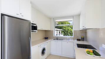 A modern kitchen with white cabinets, stainless steel appliances, a washing machine, and a fruit tray on the counter.
