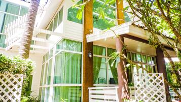 A multi-story building with large windows, a white fence, and lush greenery.