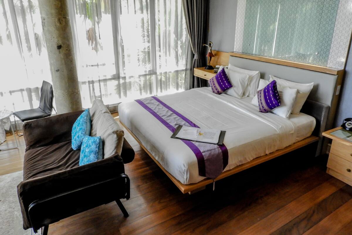 Ein Hotelzimmer mit einem großen Bett, einem Nachttisch aus Holz, einem Schreibtisch und einem Stuhl.