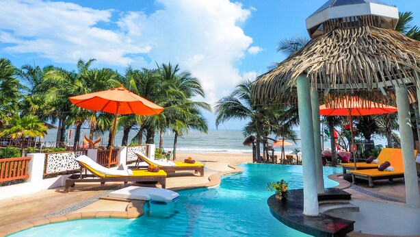A poolside area with lounge chairs, umbrellas, and a thatched structure. - Vartika Resovilla KuiBuri Beach Resort and Villas (Prachuap Khiri Khan)