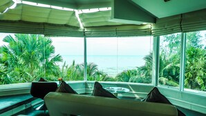 A room with a large window overlooking the ocean, a sofa with cushions, and a small table with a vase of flowers. - Vartika Resovilla KuiBuri Beach Resort and Villas (Prachuap Khiri Khan)