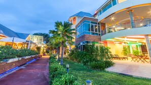 A modern hotel with a glass facade, outdoor seating, and a landscaped garden. - Vartika Resovilla KuiBuri Beach Resort and Villas (Prachuap Khiri Khan)