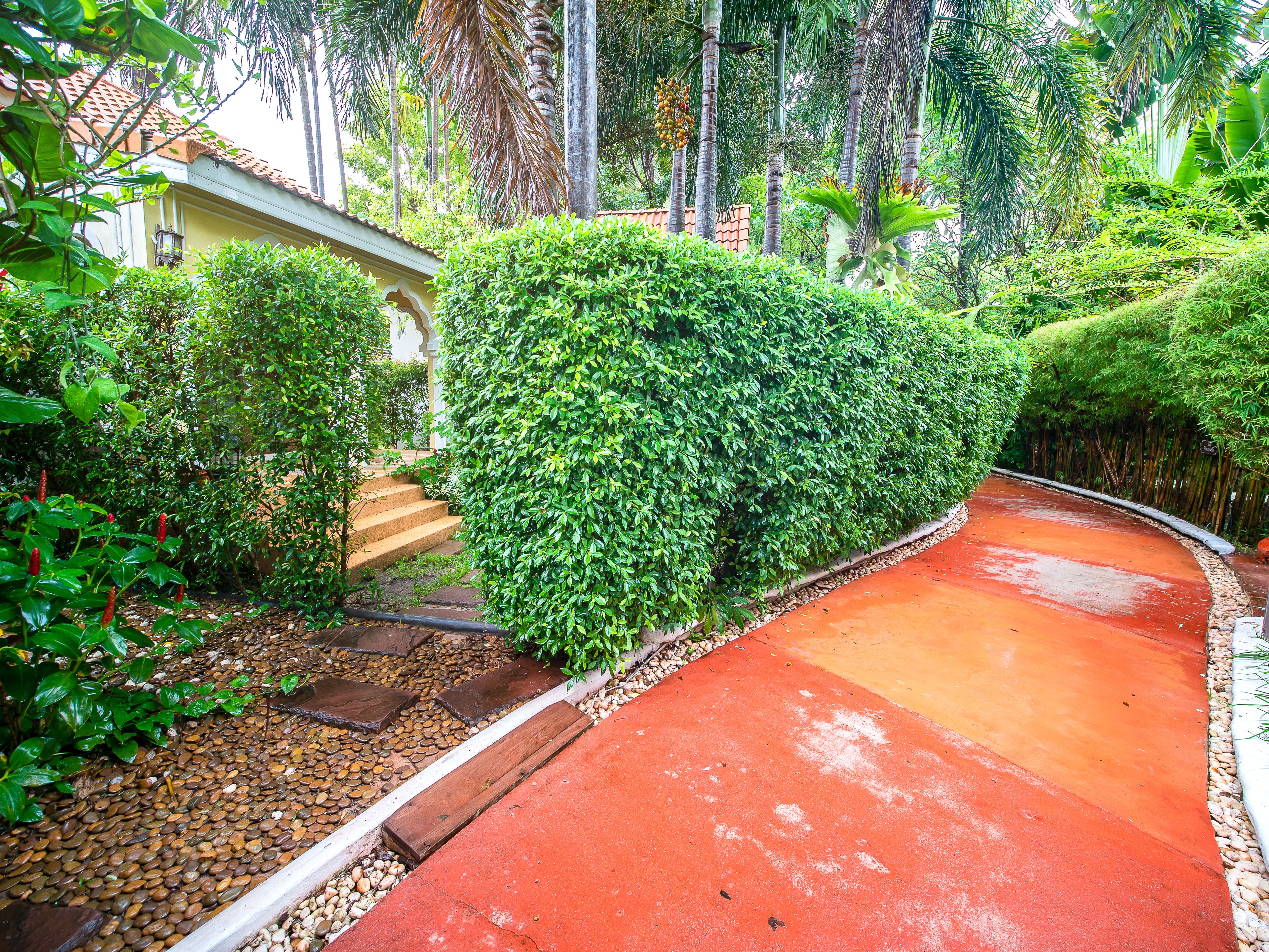 A pathway leading to a building with a tiled roof, surrounded by lush greenery and a well-maintained garden.
