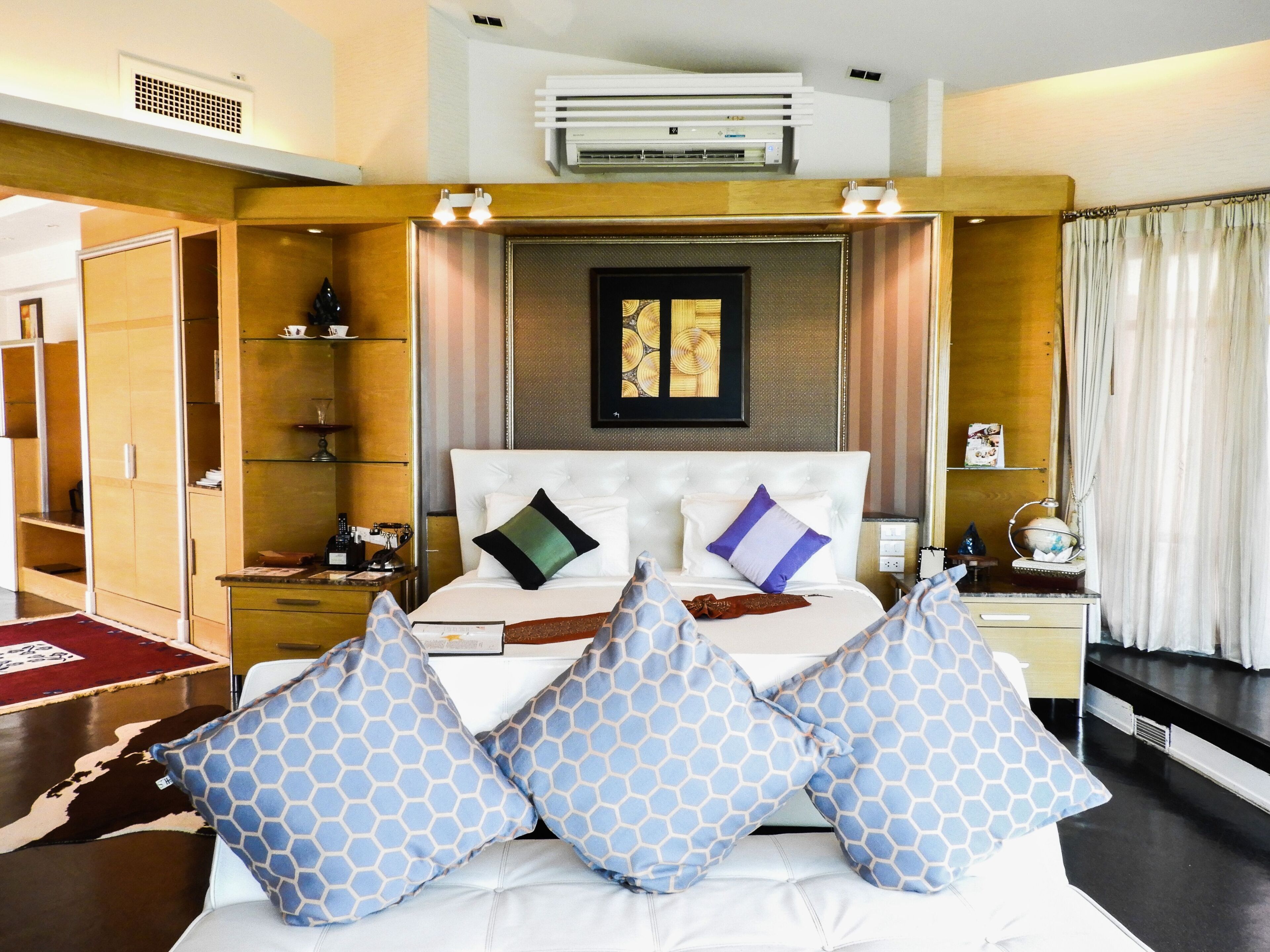 A hotel room with a bed, bedside tables, a wardrobe, and an air conditioning unit.