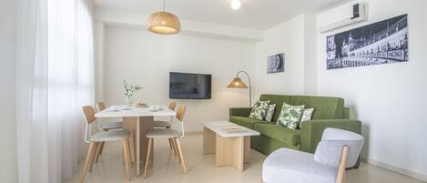 Uma sala de estar moderna com área de jantar, um sofá verde e uma TV de tela plana fixada na parede.