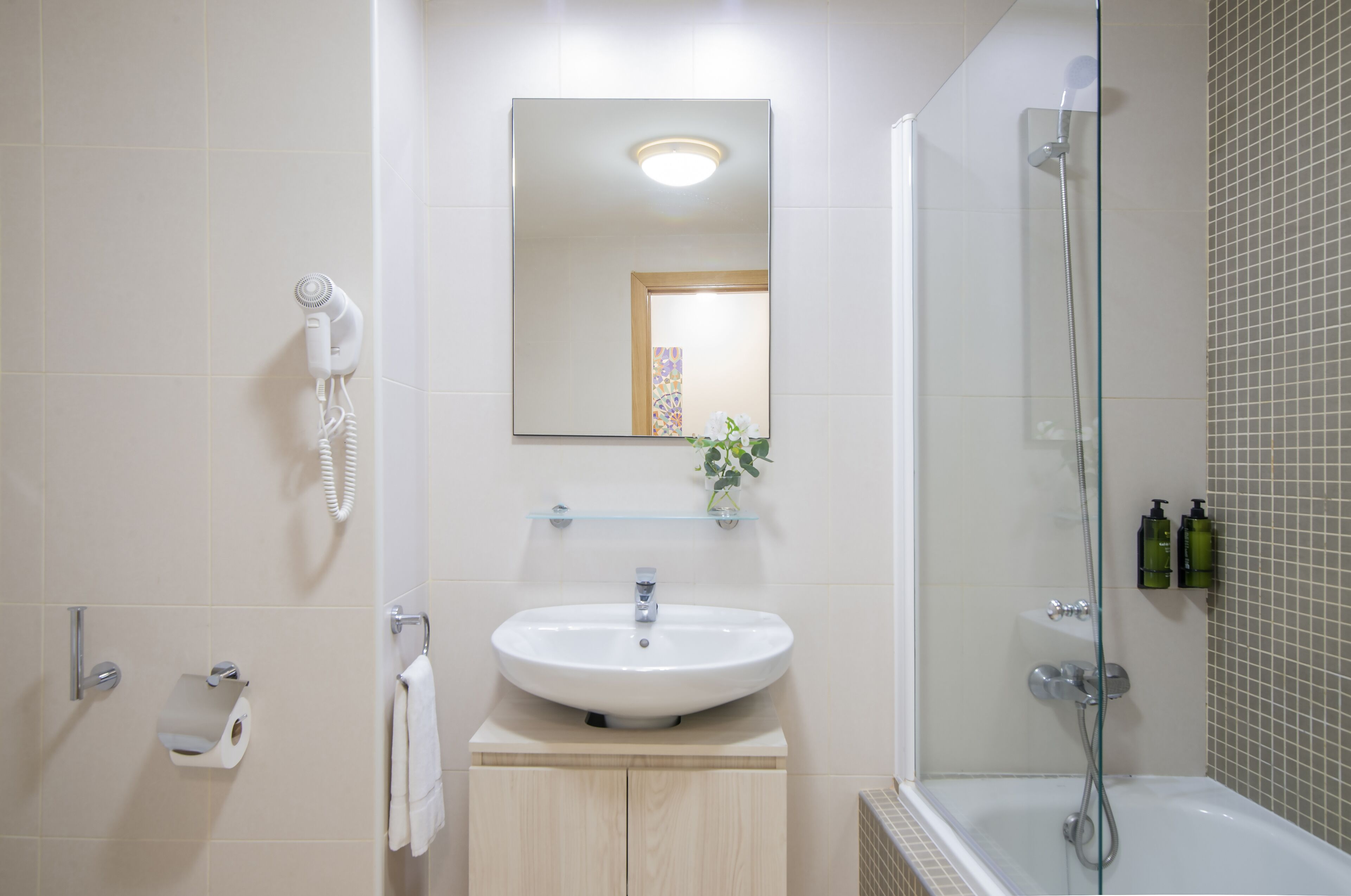 Un baño con lavamanos, espejo, secador de pelo, ducha y artículos de aseo.