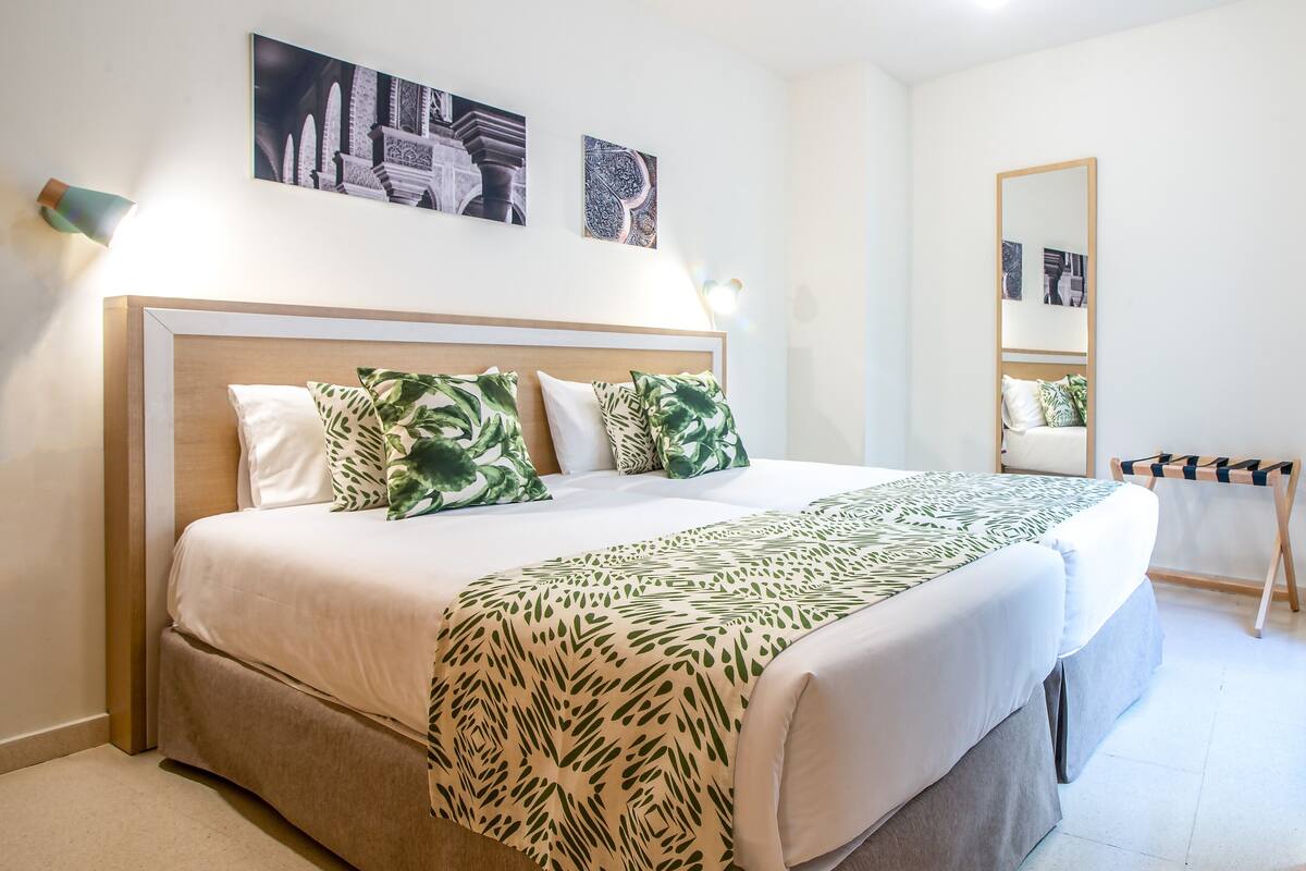 A neatly arranged bedroom with a large bed, a bedside table, a mirror, and wall art.