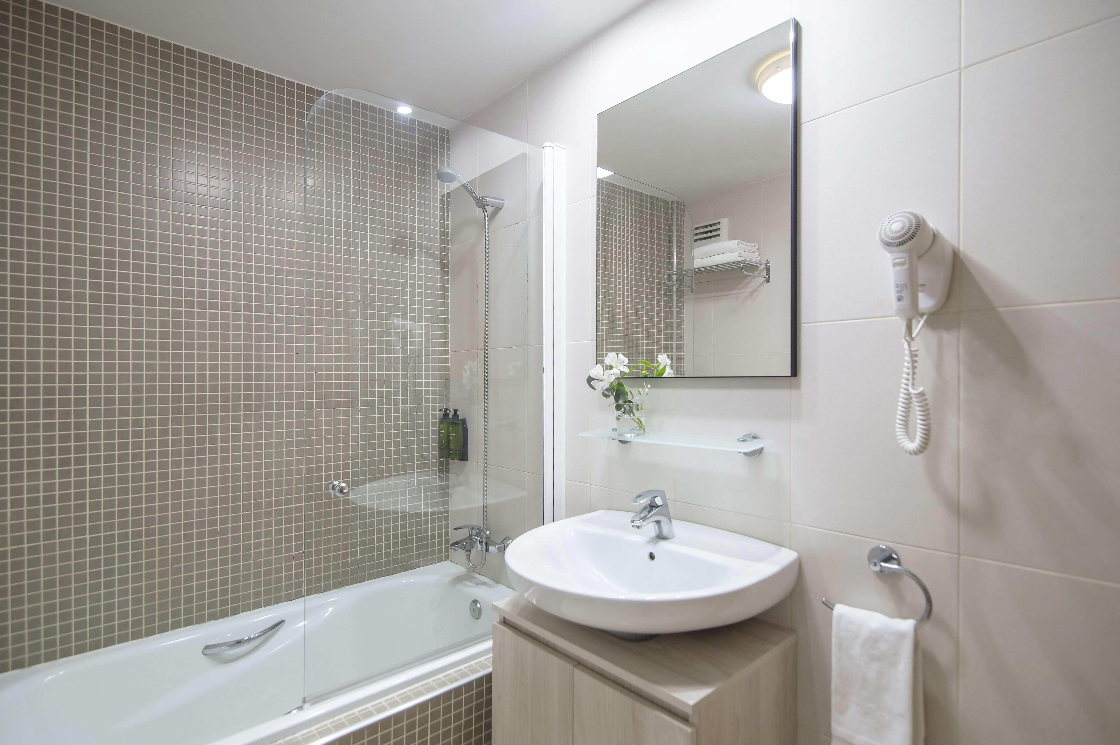 Un baño moderno con ducha envuelta en vidrio, un lavamanos blanco y un secador de pelo montado en la pared.