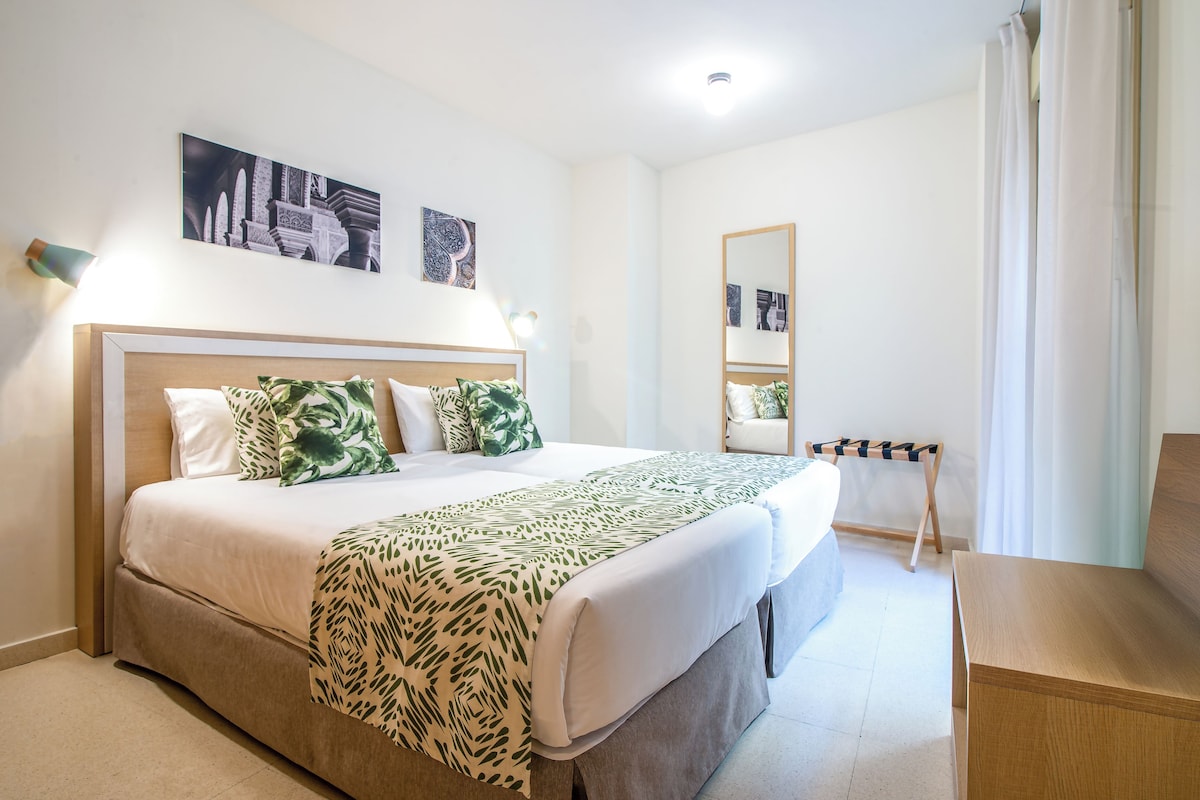 A neatly arranged hotel room with a large bed, a bedside table, a chair, and a mirror.