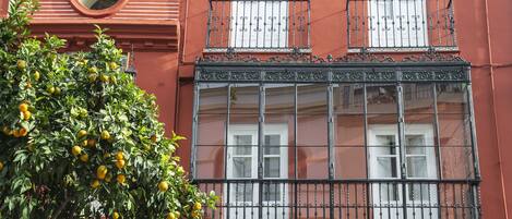 A building with a red facade, a balcony with ornate metal railings, and a window with white shutters.
