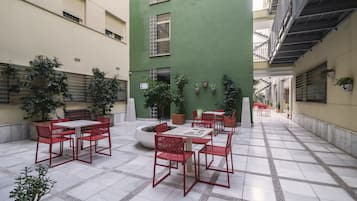 A courtyard with a dining area featuring red chairs and a white table, surrounded by potted plants and a white planter.