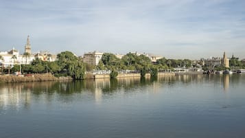 Un río tranquilo con un paisaje urbano al fondo, incluyendo edificios históricos y una torre destacada.