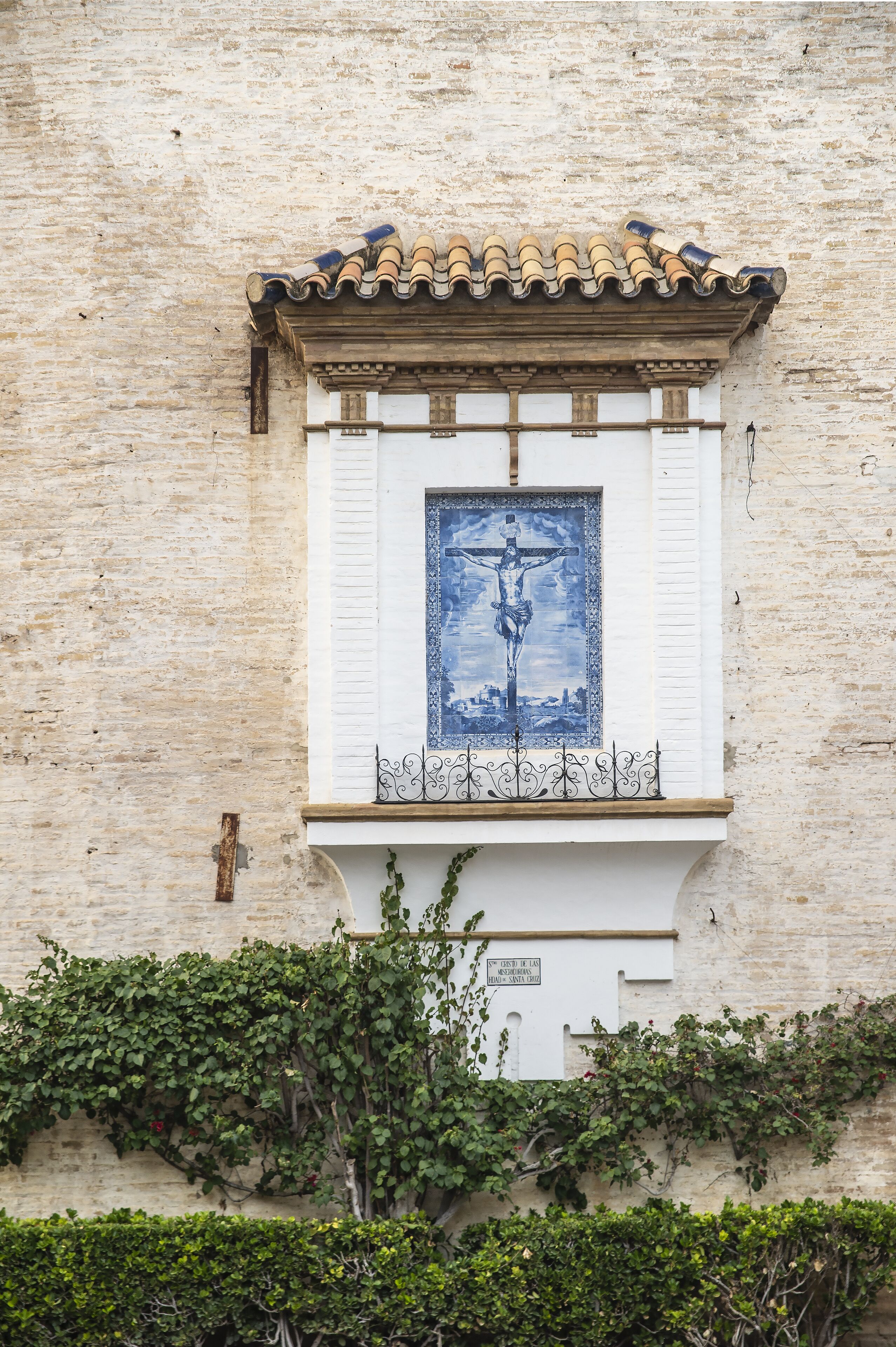 A building facade with a tiled roof, a framed picture of a crucifixion, and ivy growing on the wall.