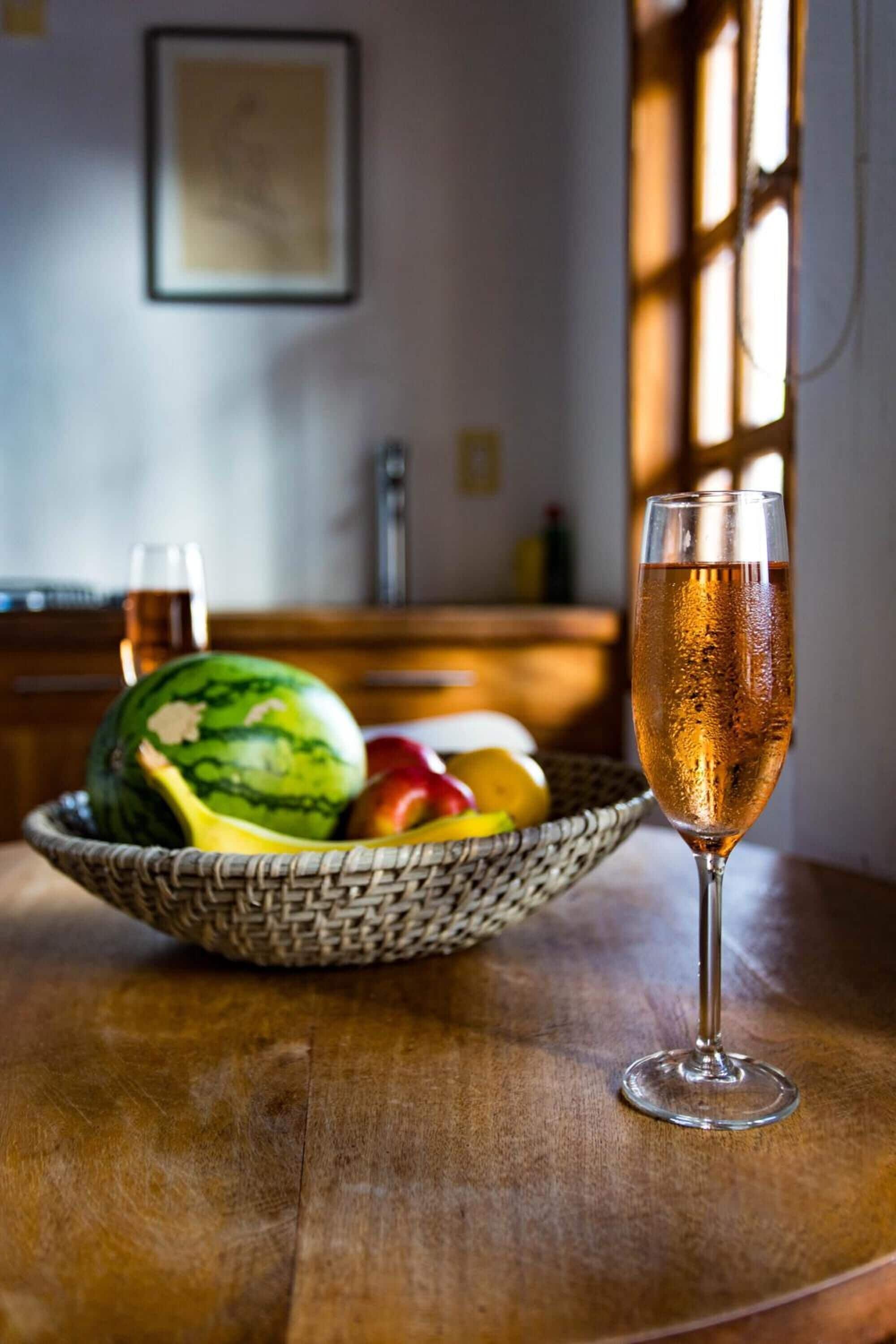 Ein Holztisch mit einem Champagnerglas, einem Obstkorb und einer Wassermelone.