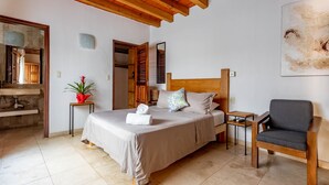 A bedroom with a bed, bedside tables, a chair, a potted plant, and a painting on the wall. - Olas Altas Suites (Puerto Vallarta)