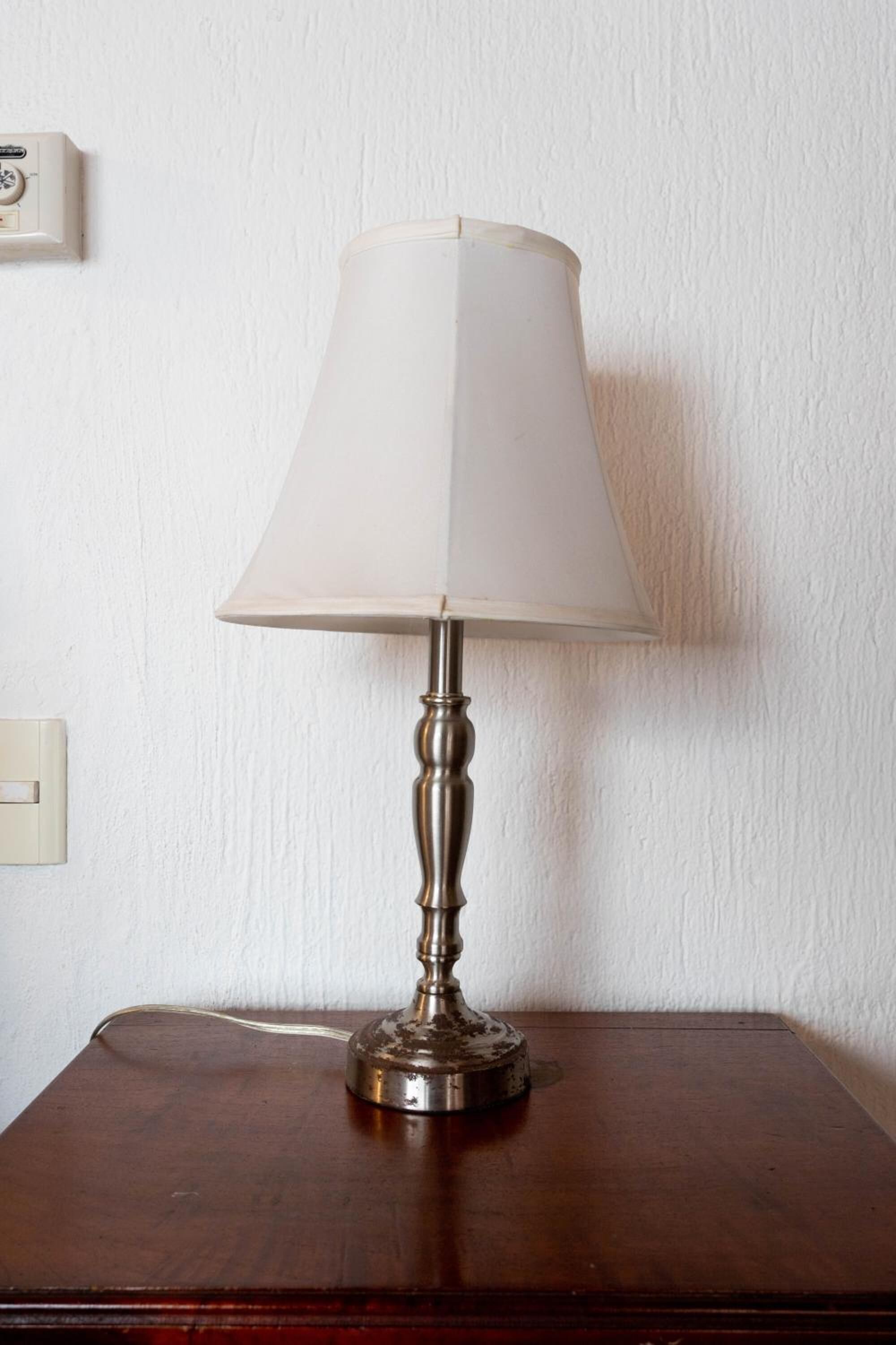 A table lamp with a white shade on a wooden table against a white wall.