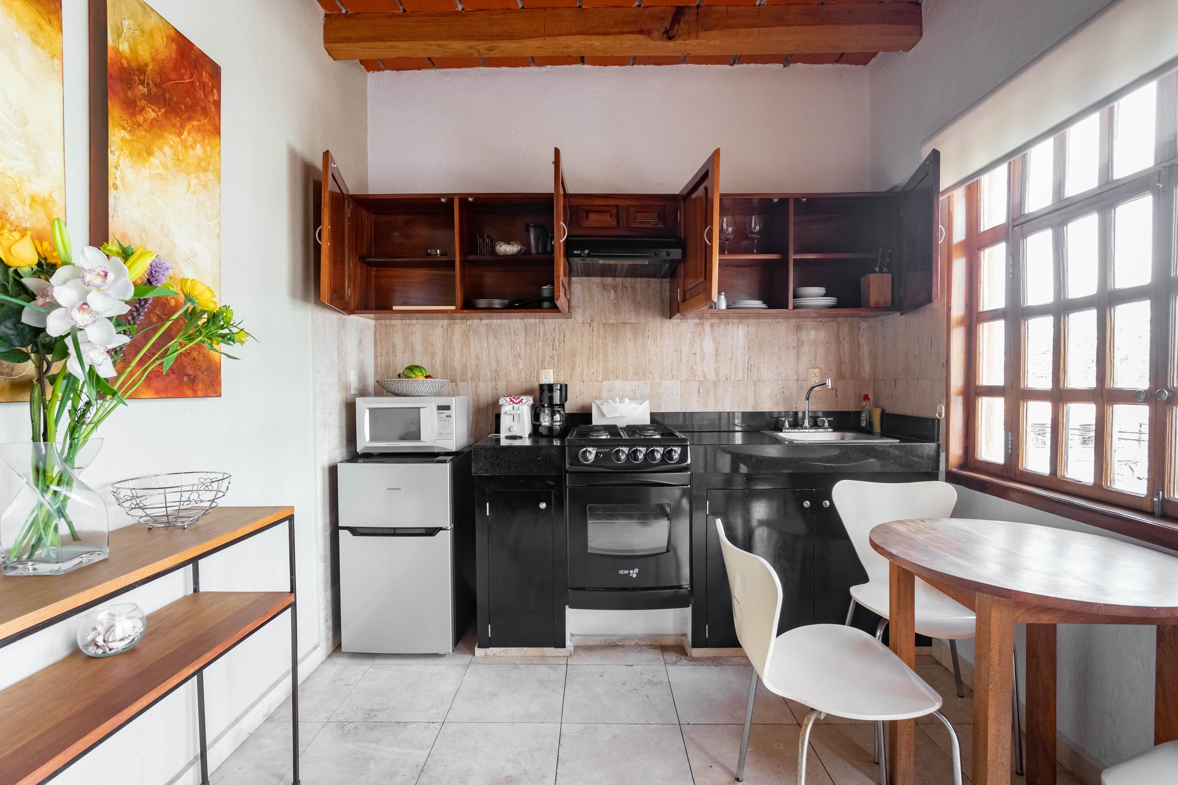A compact kitchen with a stove, microwave, and cabinets. There is a dining table with chairs and a vase of flowers on the counter.