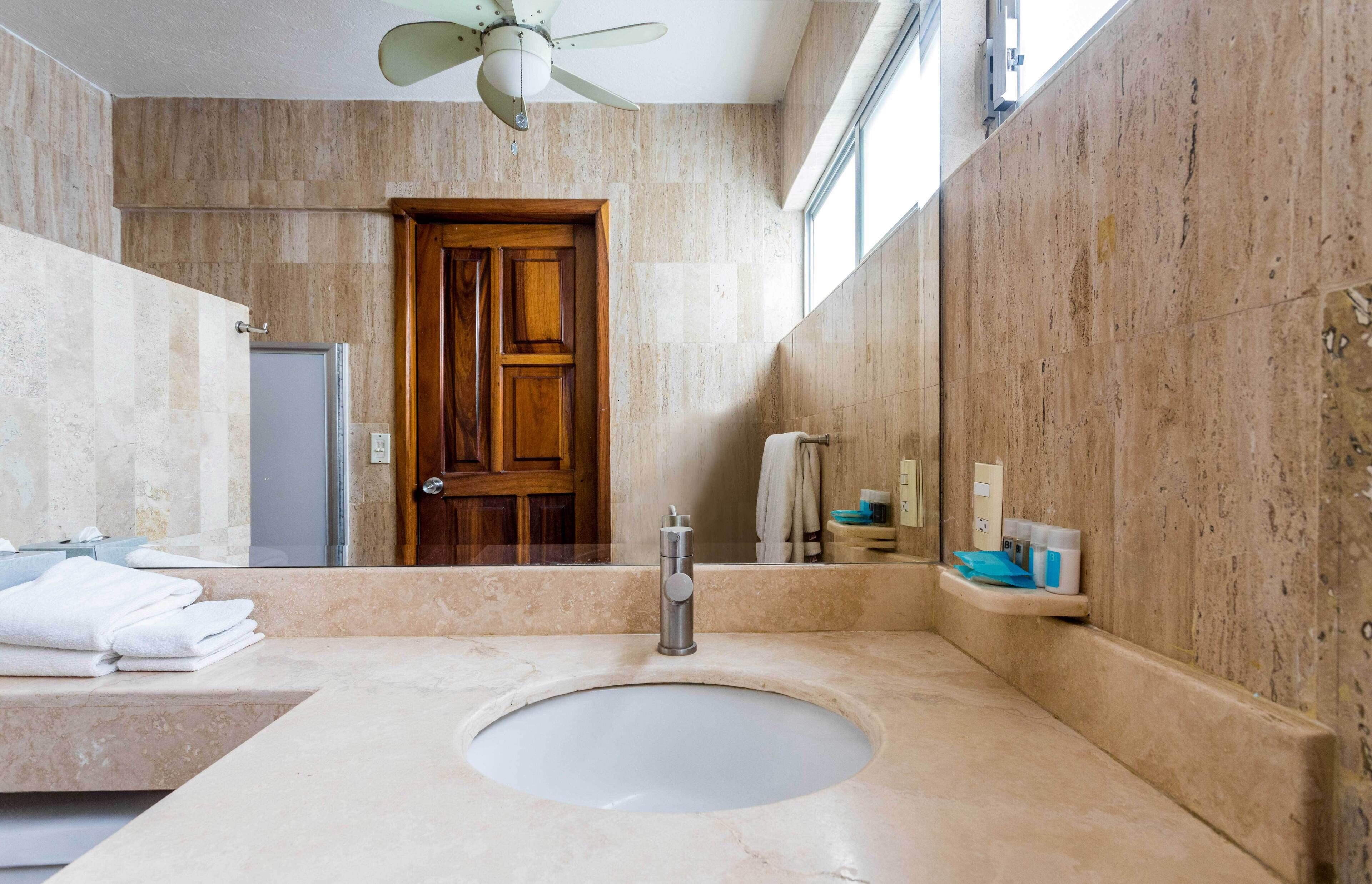 Une salle de bain avec un lavabo en marbre, une porte en bois et un ventilateur de plafond.