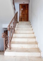 Una escalera con baldosas color crema y barandilla de metal marrón que conduce a una puerta de madera.