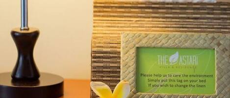 A bedside table with a lamp, a tissue box, and a tag instructing to help care for the environment.