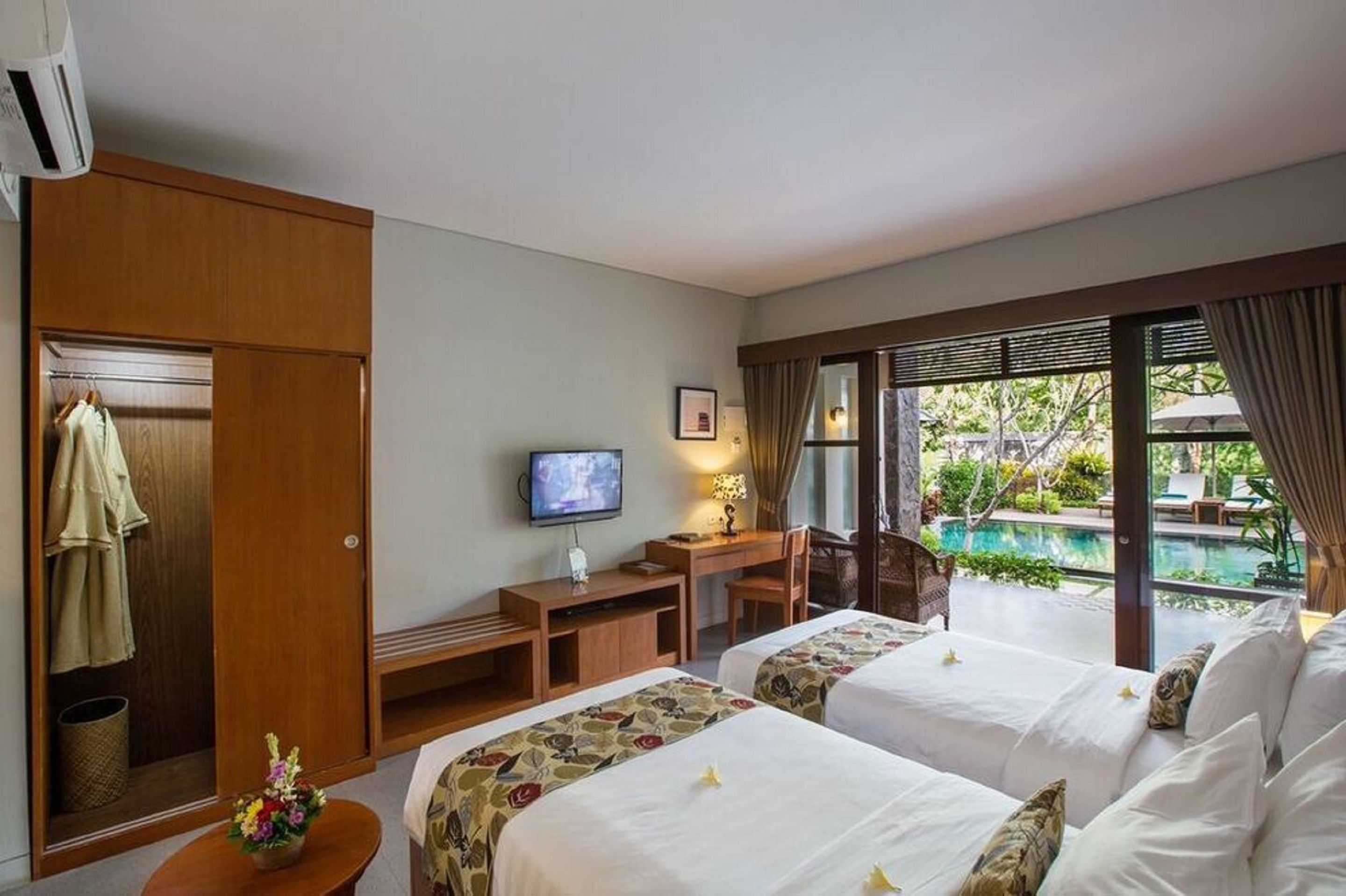 A hotel room with two beds, a desk with a TV, a window with a view of a pool, and a wardrobe.