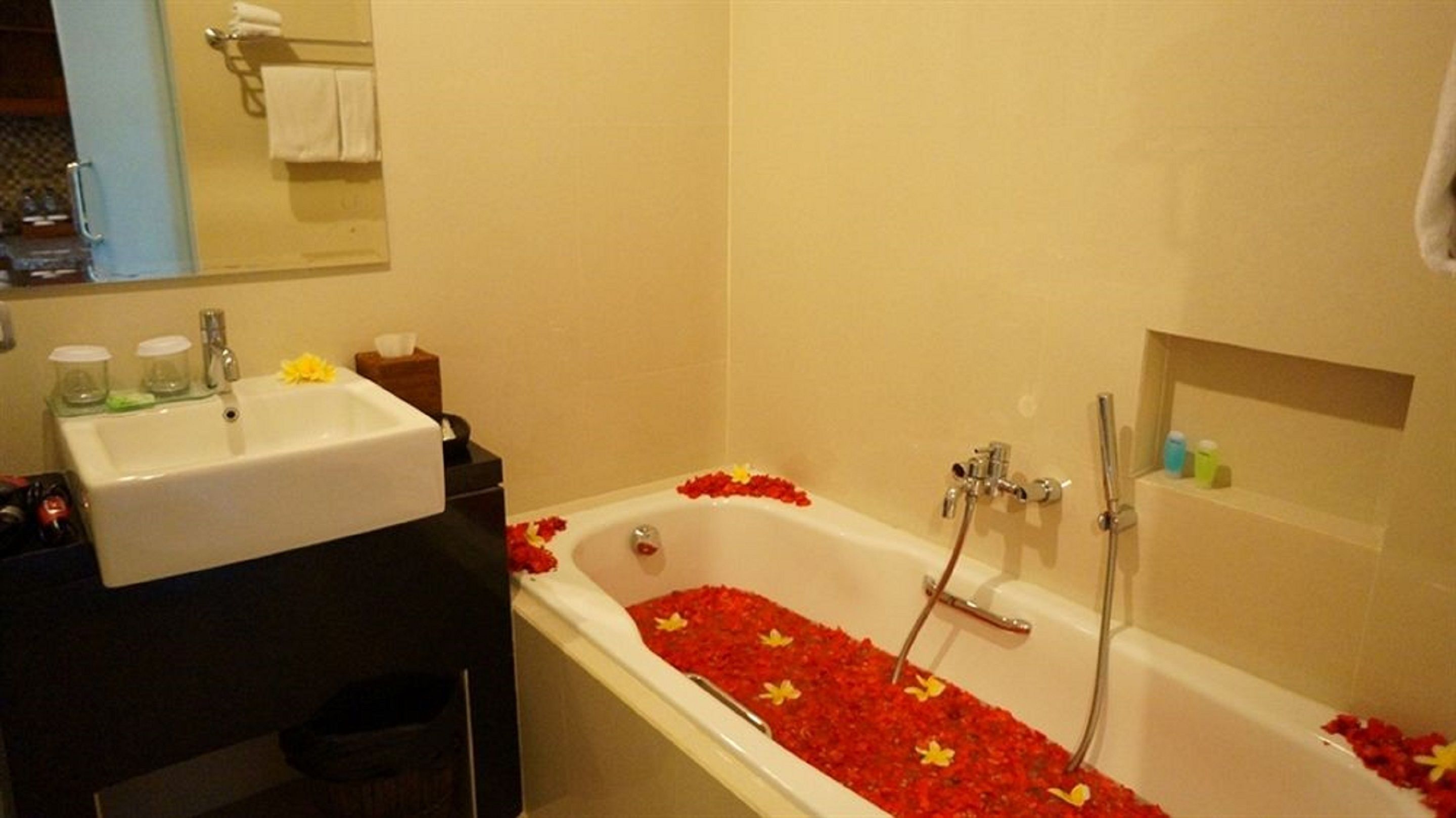 Un baño con una bañera llena de pétalos de rosa, un lavamanos y un espejo.