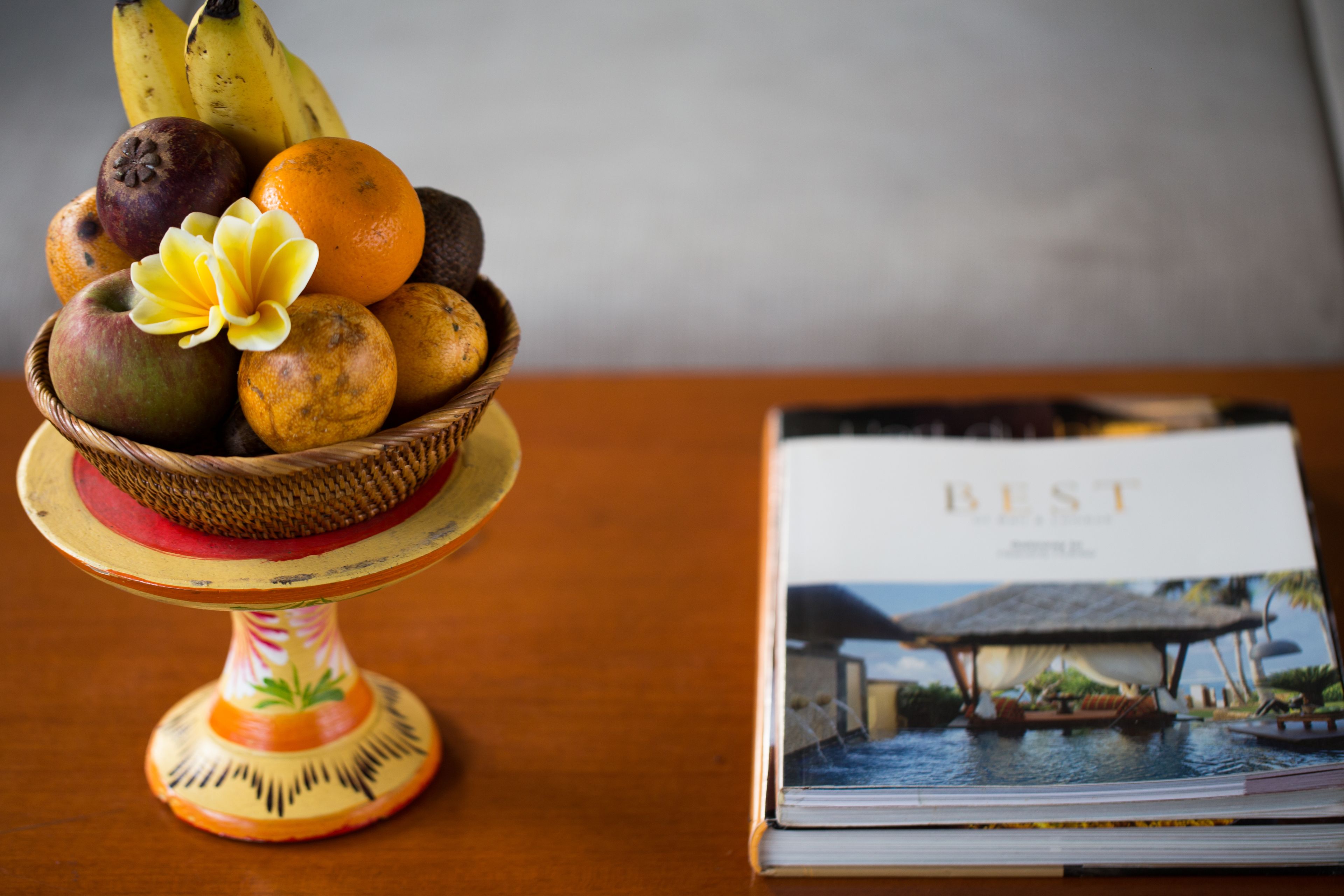 A fruit bowl with a decorative base on a wooden table next to a book titled "BEST".