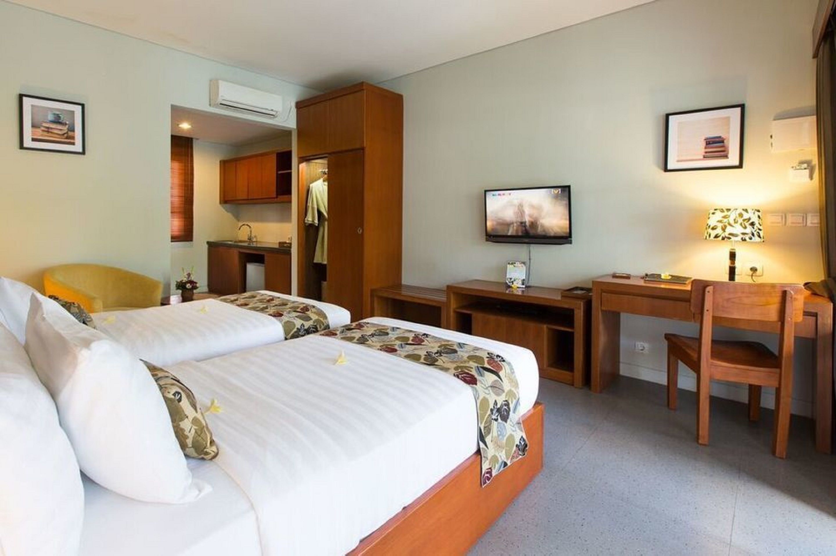 A hotel room with two beds, a desk, a chair, a television, and a kitchenette.