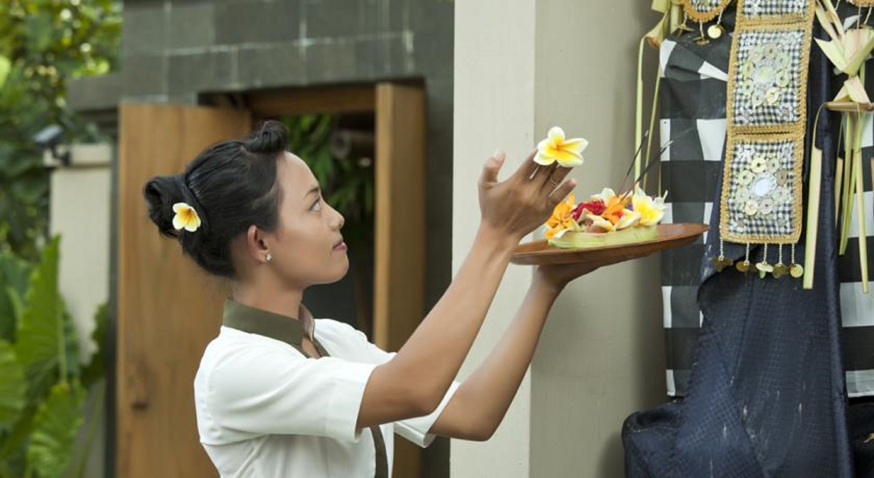 A person holding a tray with flowers and a decorative item, standing in front of a wall with hanging decorations.