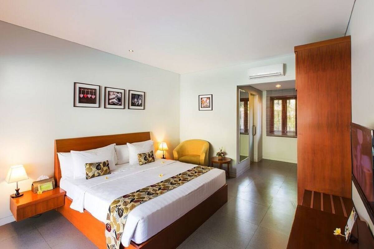 Una camera d'albergo con un letto grande, un comodino con una lampada, una sedia e una televisione.