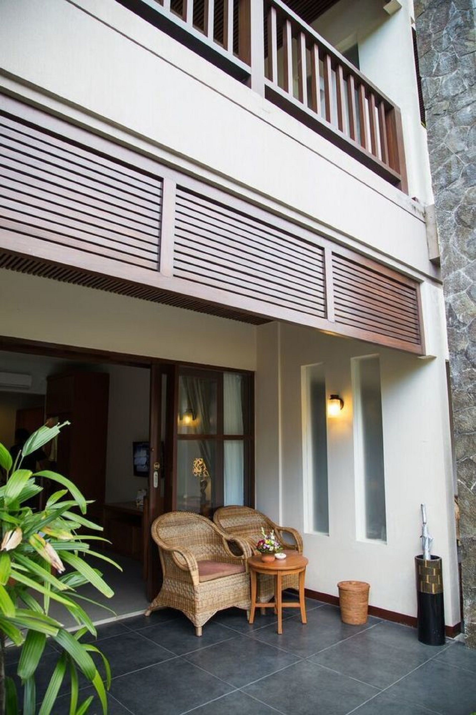 A two-story building with a balcony, a door with glass panels, and a small outdoor seating area with wicker furniture.