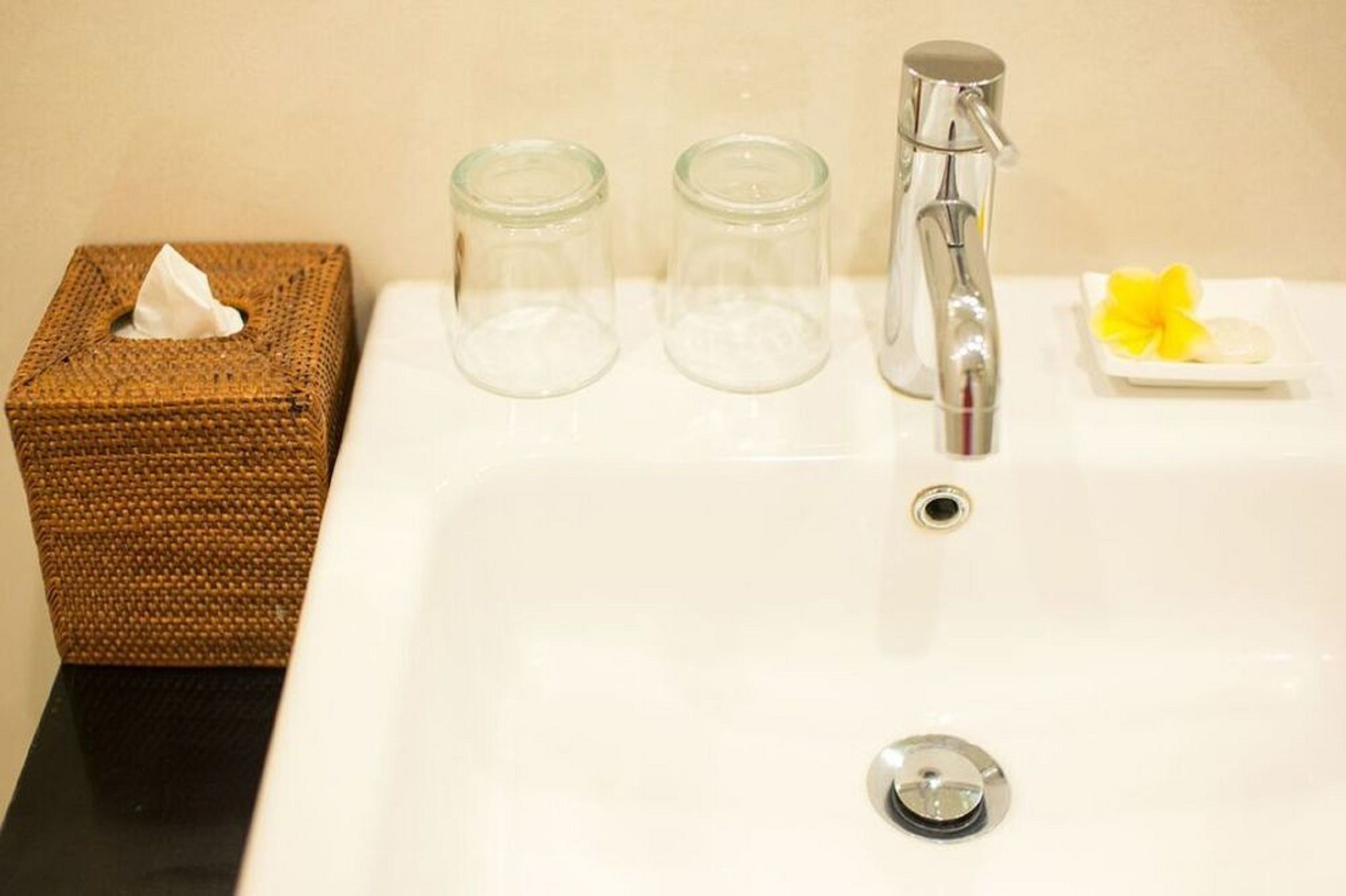 Un lavabo de salle de bain avec un boîte de mouchoirs, deux pots en verre et une fleur.