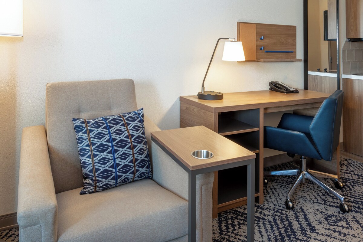 A hotel room with a sofa, a desk with a lamp, a chair, and a small table.