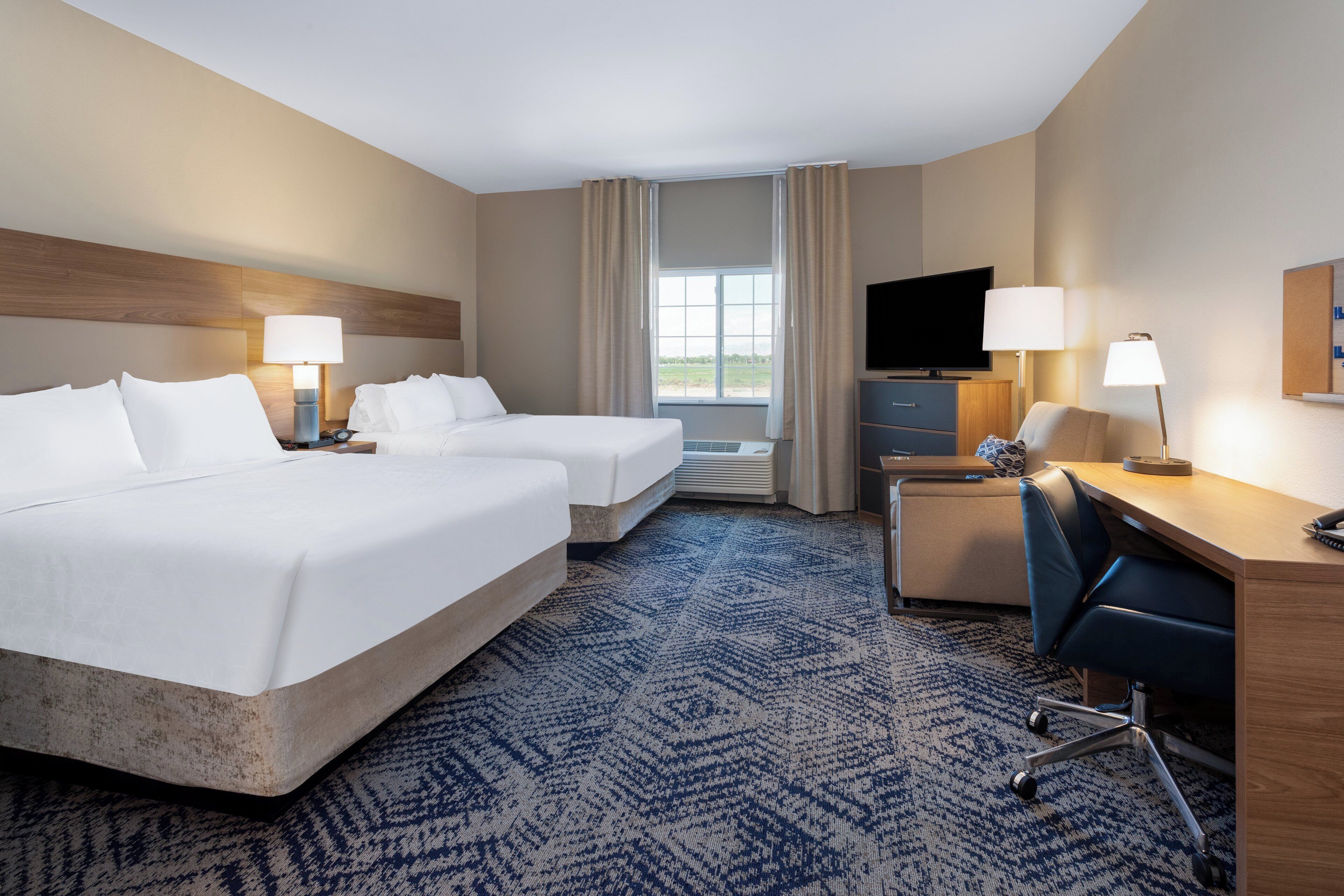 A hotel room with two beds, a desk, a chair, a television, and a window with curtains.